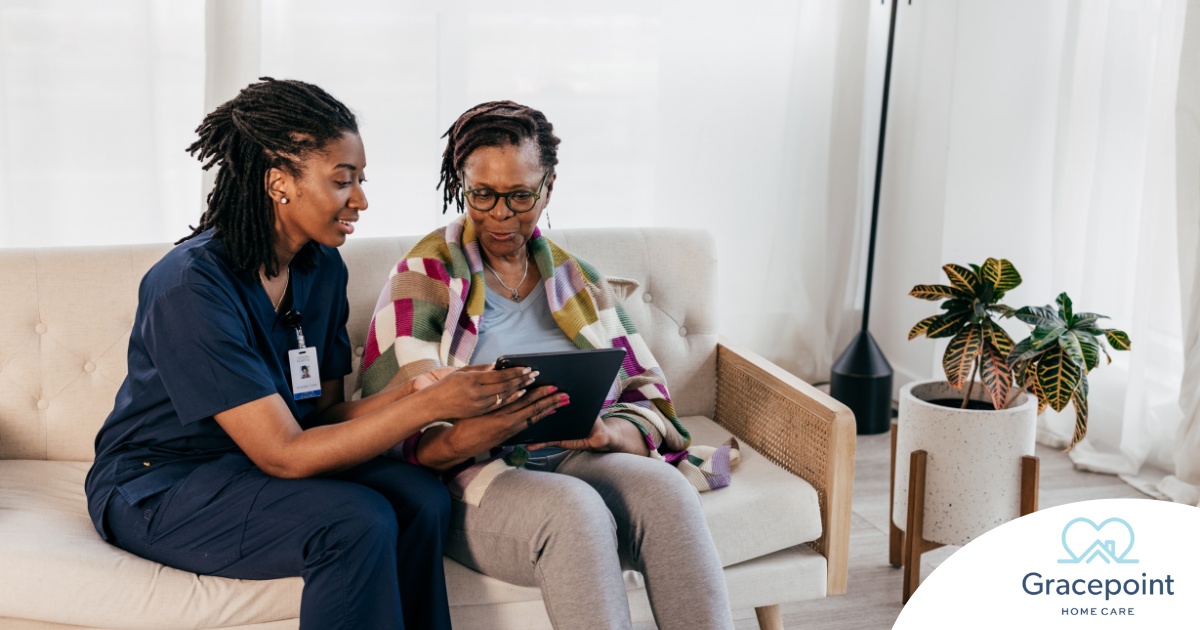 A caregiver talks with a patient while showing her information on a tablet representing the type of thorough communication needed for effective and professional care of home health care patients.