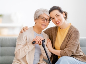 A care giver puts her arm around an elderly patient sitting on a couch.