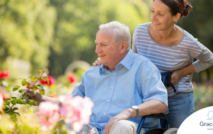 A caregiver brings an older adult with a wheelchair to see some flowers representing how professional caregivers can make outdoor activities accessible.