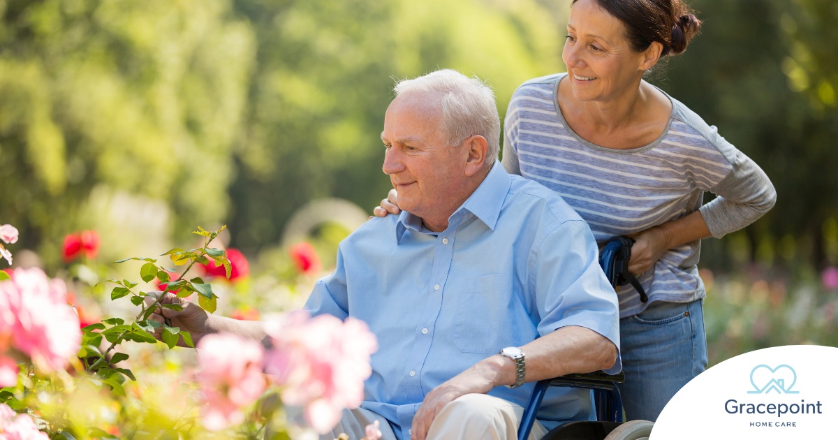 A caregiver brings an older adult with a wheelchair to see some flowers representing how professional caregivers can make outdoor activities accessible.