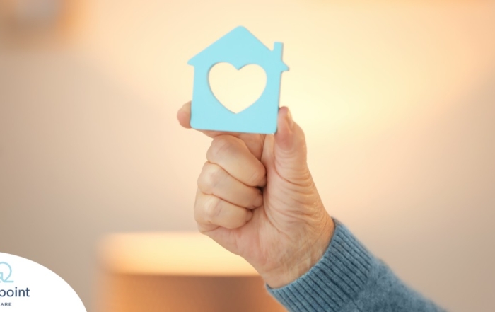 A hand holds up a cutout of a home with a heart in it, representing the home care industry.