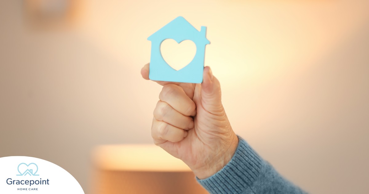 A hand holds up a cutout of a home with a heart in it, representing the home care industry.