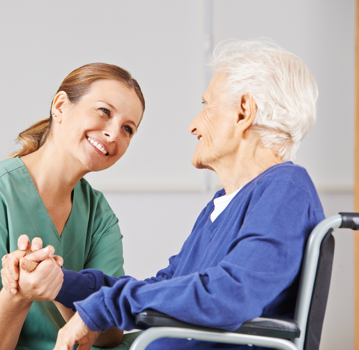 Companion Care in Gulf Shores (2) A caregiver with a ponytail gently holds the hand of a senior woman in a wheelchair, offering support and showing compassion.