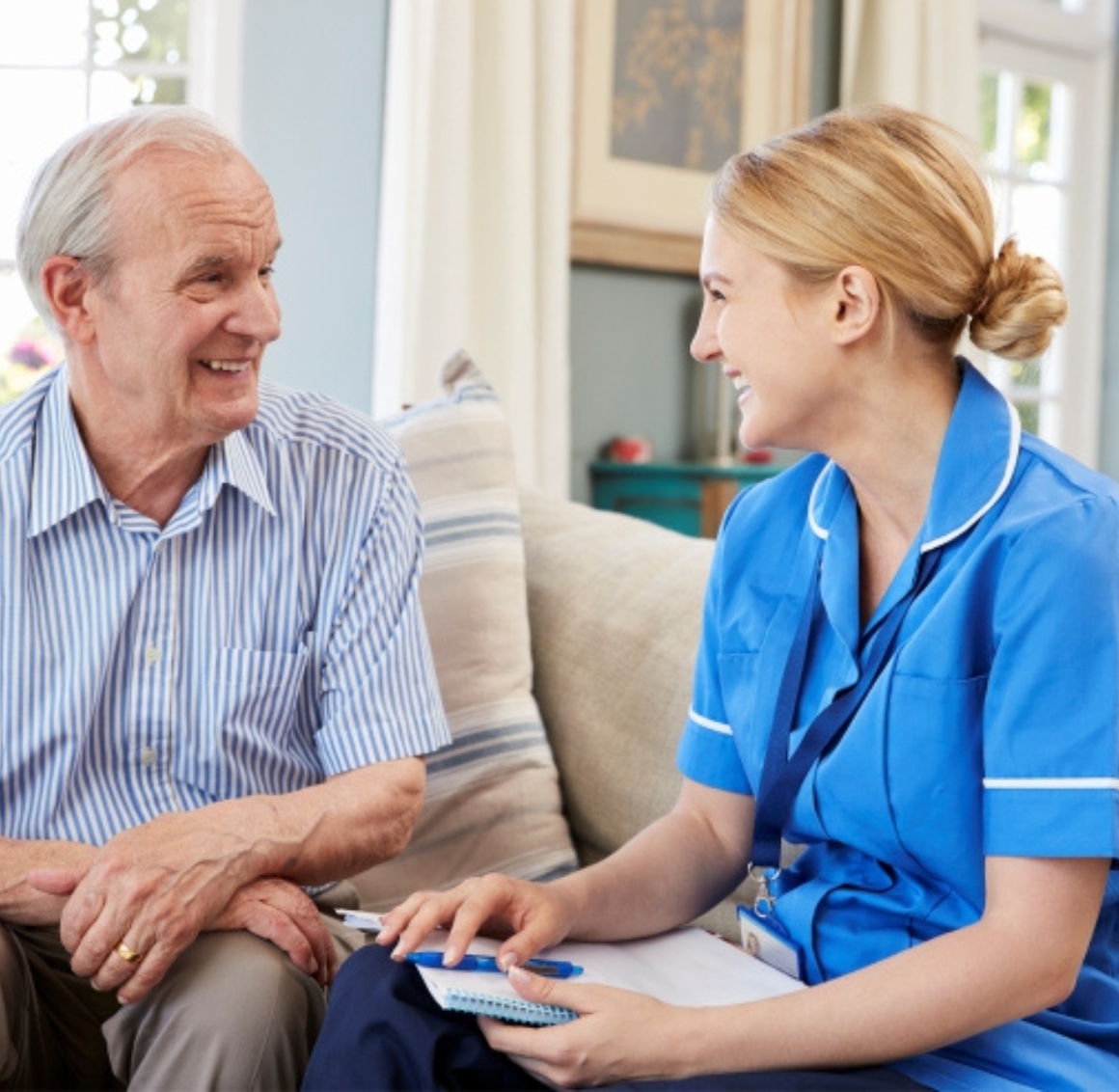 A female caregiver with a bun discusses senior care with a senior, both sitting and facing each other, engaged in a thoughtful conversation.