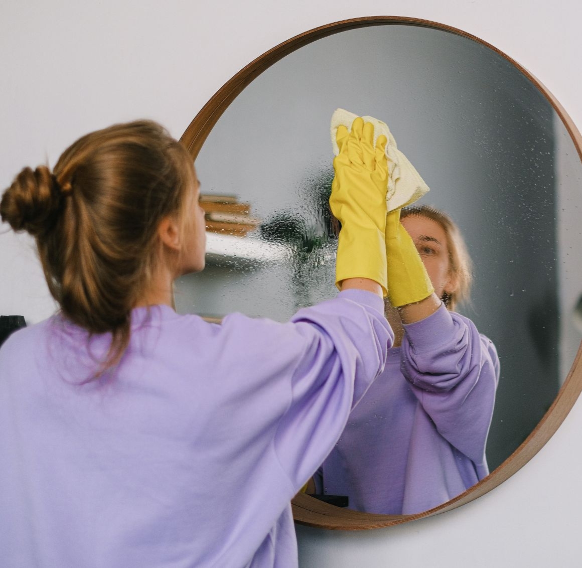 A woman cleaning a mirror in a bright, tidy living room, representing light housekeeping in Gulf Shores.