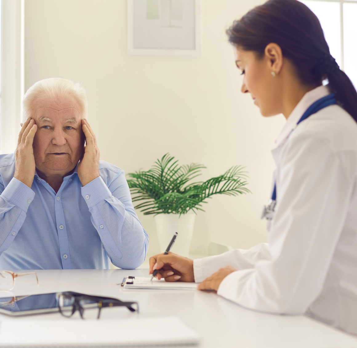 A female caregiver in white scrubs provides medication supervision in Gulf Shores, taking the medical history of a senior man in a comfortable home setting.