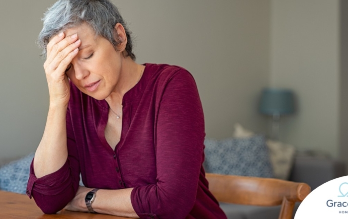 A woman holds her head in her hand, representing the stress that new family caregivers go through.
