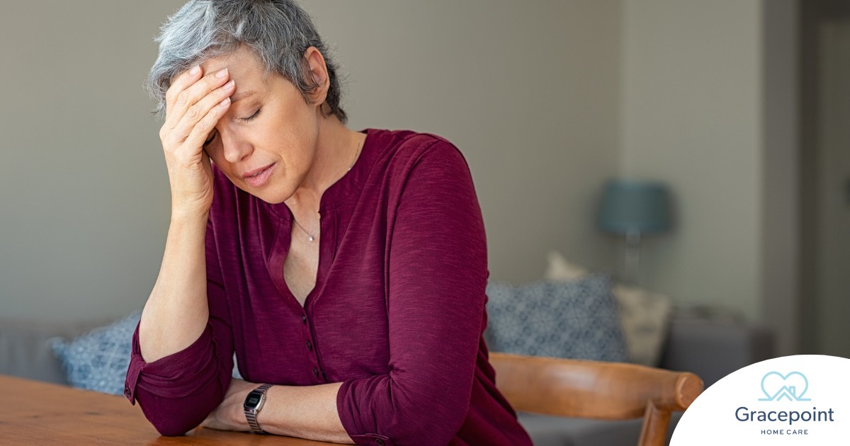 A woman holds her head in her hand, representing the stress that new family caregivers go through.