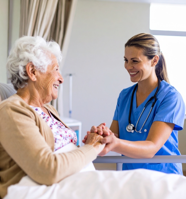 Add-on Nursing Support Services (1) A compassionate nurse in blue scrubs providing Add-on Nursing Support Services, holding hands and smiling warmly at a senior woman in bed.