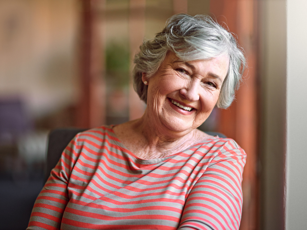 Smiling older woman sitting by a window, representing independence and peace of mind with GraceLink Care Connect from Gracepoint Home Care.