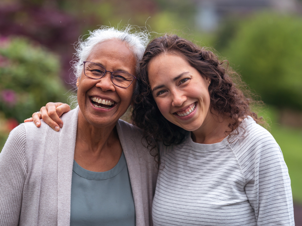 Elderly woman and her adult daughter smiling together outdoors, representing how GraceLink Care Connect from Gracepoint Home Care helps reduce caregiver stress and strengthen family bonds.