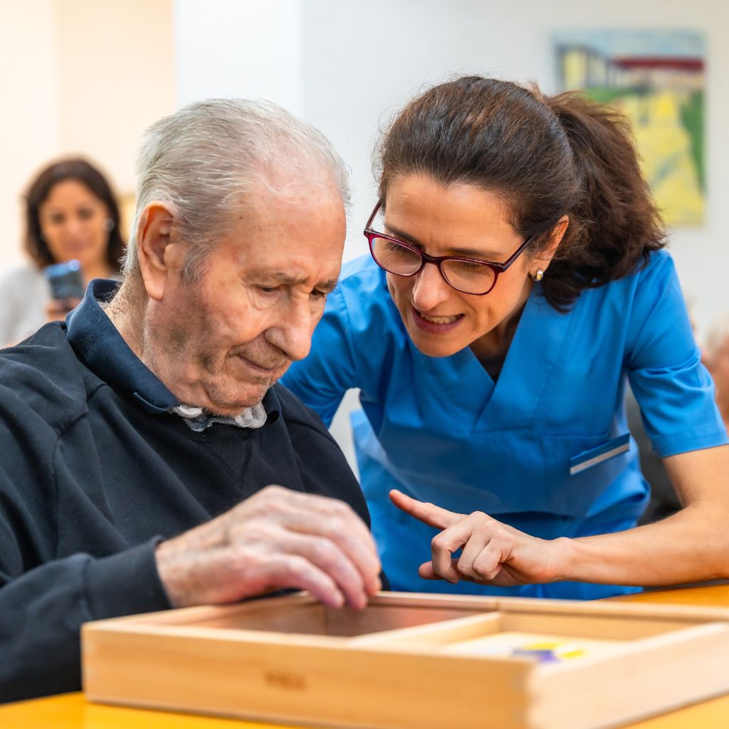 Caregiver providing gentle memory care support to an elderly man during a cognitive activity